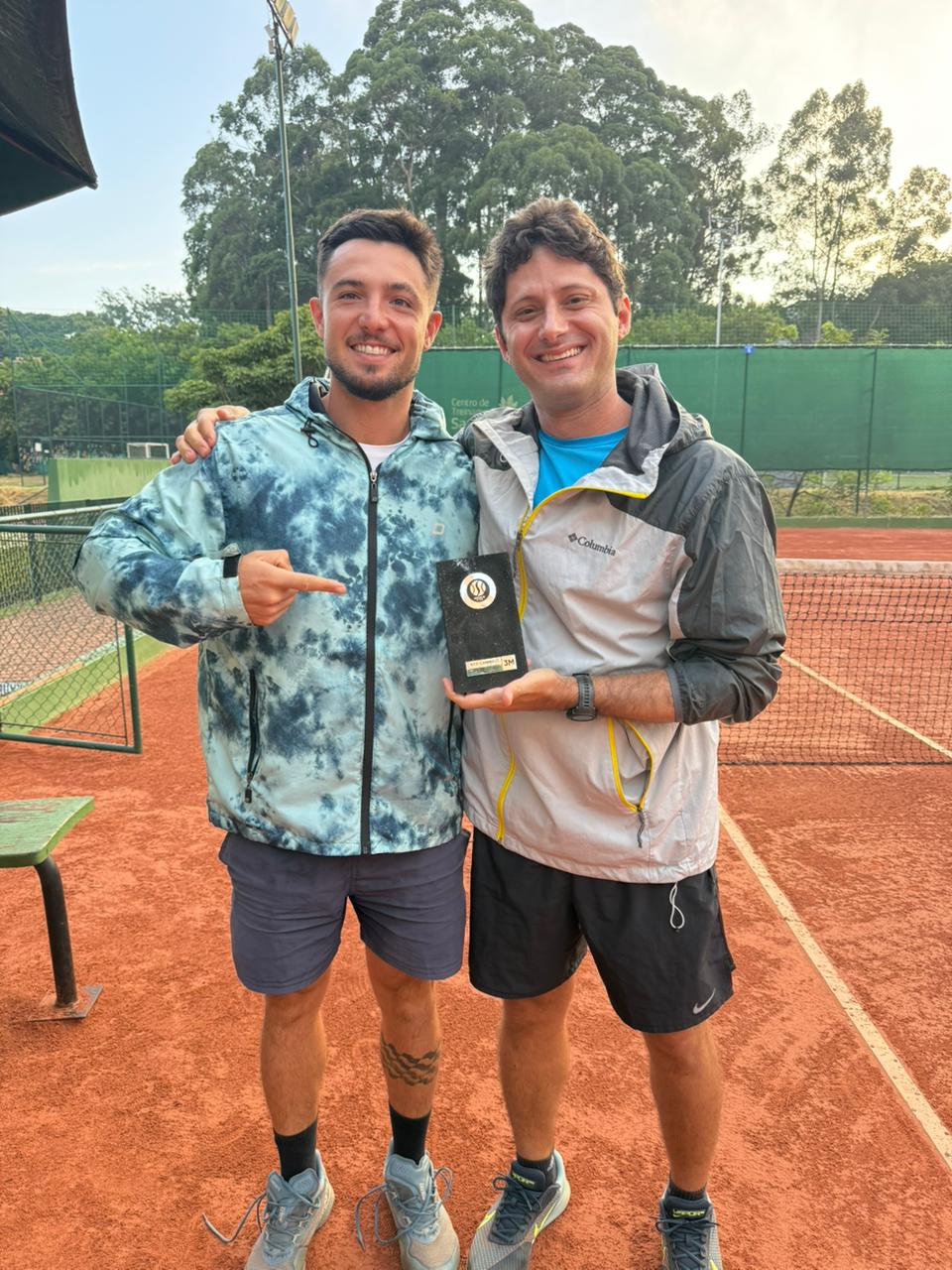 Aluno campeão em quadra de saibro segurando troféu